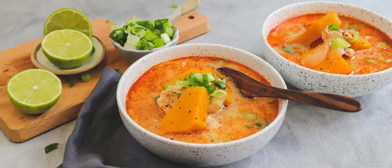 Two bowls of Thai style chicken and pumpkin soup with fresh cut limes